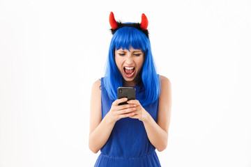 Portrait of angry woman wearing blue wig and toy devil horns screaming while holding cellphone