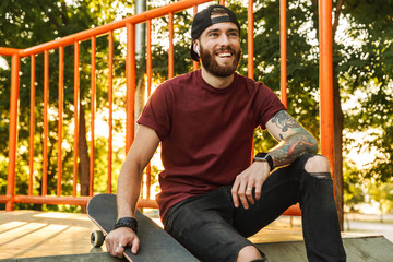 Attractive cheerful young man sitting at the skate park ramp