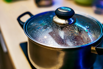 Metal pan with misted lid. Water droplets on the dishes during cooking on the electric stove. Close up. The view from the top.