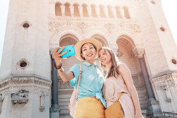 Wall Mural - Two Happy women friends travelers taking selfie in front of the Cathedral of Notre Dame de Fourviere in Lyon city, France. Tourism and religion concept
