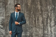 © Friends Stock - Great style. Confident bearded businessman in full suit looking away while standing against grey stone wall outdoors