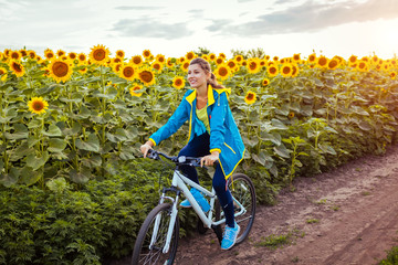 Wall Mural - Young happy woman bicyclist riding bicycle in sunflower field. Summer sport activity. Healthy lifestyle