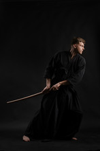 Kendo Guru Wearing In A Traditional Japanese Kimono Is Practicing Martial Art With The Shinai Bamboo Sword Against A Black Studio Background.