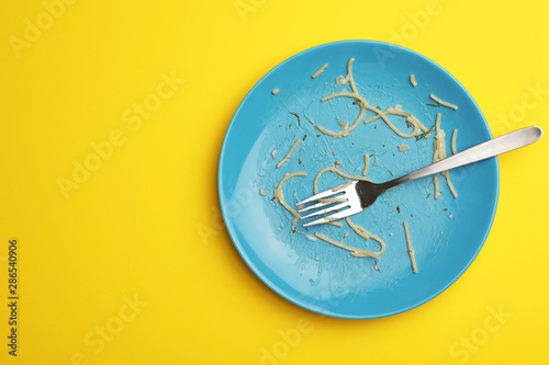 Cuadros en Lienzo Dirty plate with food leftovers and fork on yellow background, top view