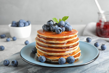 Plate of delicious pancakes with fresh blueberries and syrup on grey table against light background