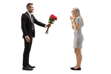 Wall Mural - Young man smiling and giving a bunch of red roses to a surprised woman