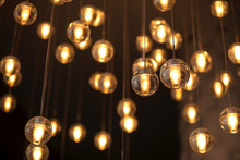 Decorated Electric Garland For Lighting With Bulbs Warm White And Yellow Light On A Dark Background. Blurred Background. Bulbs In The Interior Decor