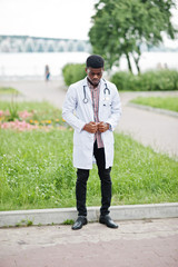 Wall Mural - Young african american male doctor in white coat with a stethoscope posed outdoor.