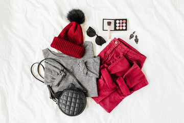 Vinous winter hat and trousers with gray  sweater, handbag on white sheet. Women's stylish autumn or winter outfit. Trendy  clothes collage. Flat lay, top view.