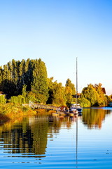 Autumn time, Marina near the riverbank overgrown with yellowed trees, parking for two yacht against the blue sky