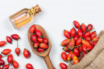 Glass bottle of rosehip seed essential oil with fresh rose hip fruits on white rustic background. Dogrose oil with fresh dog roses