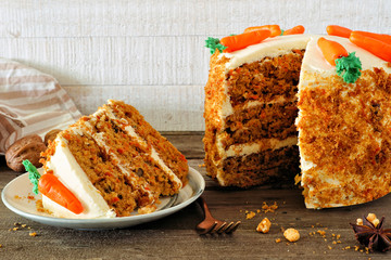 Wall Mural - Slice of homemade carrot cake with cream cheese frosting and fondant carrots. Side view table scene with a white wood background.