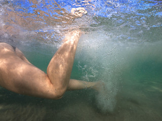  Unidentified woman's feet underwater swimming with effort and releasing air bubbles to reach the shore