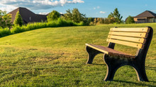 Panorama Frame Empty Bench On A Grassy Hill Against Homes And Cloudy Blue Sky On A Sunny Day