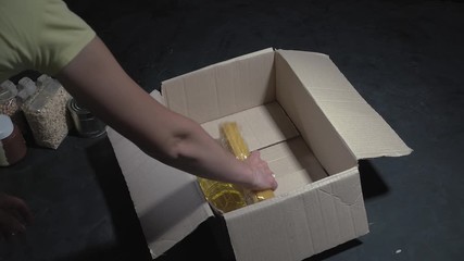 Canvas Print - Female hands packing a box of different products on dark background
