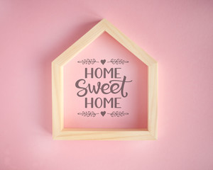 Wooden frame in the shape of a house on pink background with text