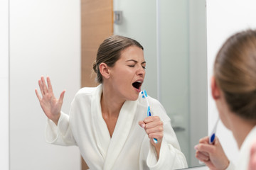 Wall Mural - Woman in white bathrobe holding toothbrush, standing in bathroom