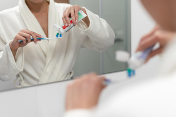 Wall Mural - Woman in white bathrobe holding toothbrush, standing in bathroom