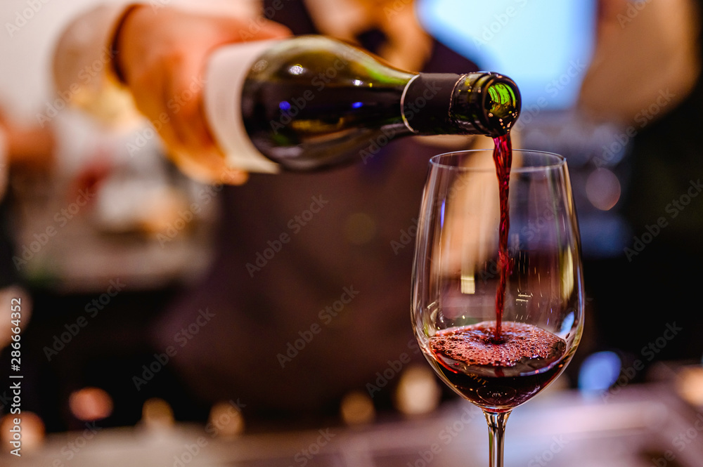 Pouring glass of red wine from a bottle. - obrazy, fototapety, plakaty 
