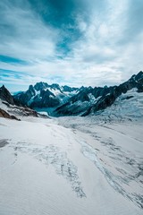 Poster - Vertical shot of a snowy hill with mountains in the distance under a cloudy sky