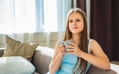 portrait of young teenager brunette girl with long hair sitting on sofa with cup at home