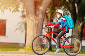 Wall Mural - Child with rucksack riding on bike in the park near school