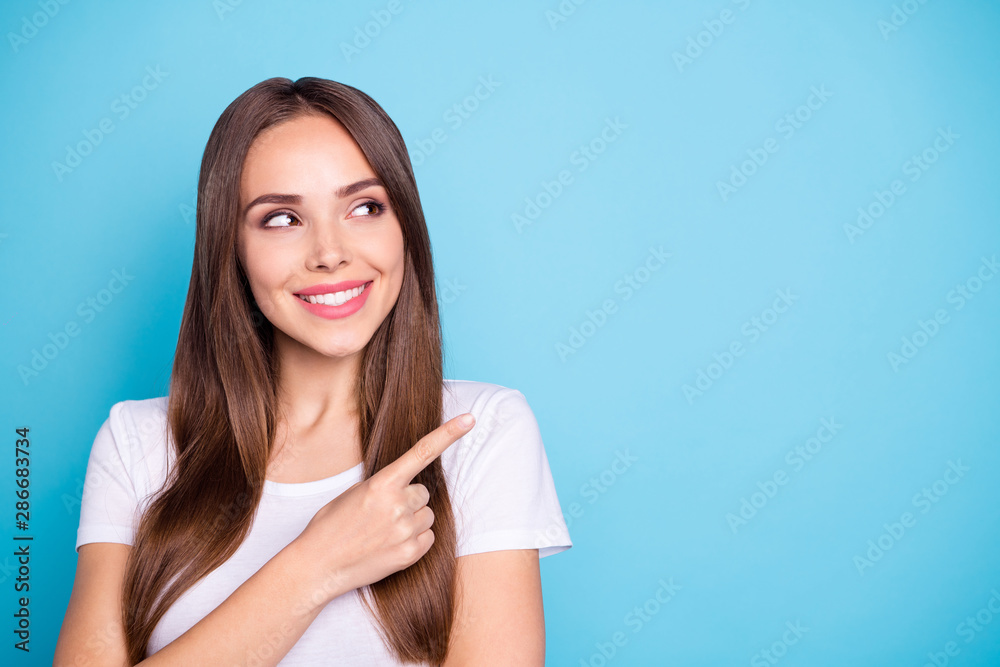 Close up photo of lovely youth pointing at copy space looking smiling wearing white t-shirt isolated over blue background - obrazy, fototapety, plakaty 