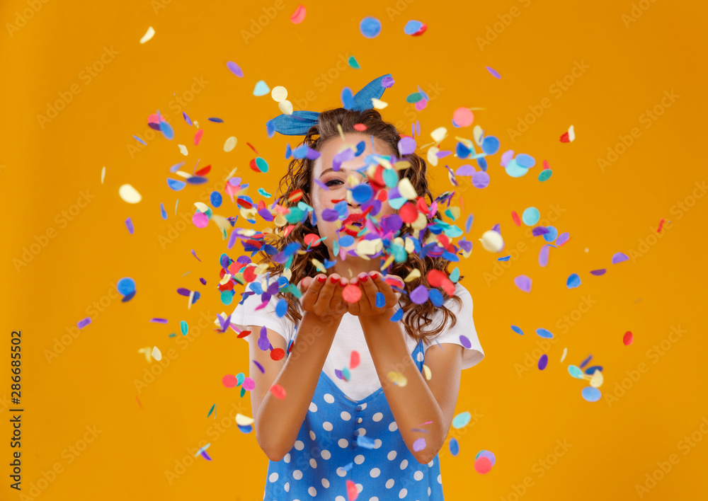 cheerful funny young woman with festive confetti on yellow . - obrazy, fototapety, plakaty 