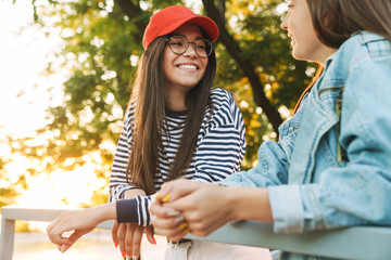 Sticker - Image of two happy girls smiling and talking while bending on railing in green park