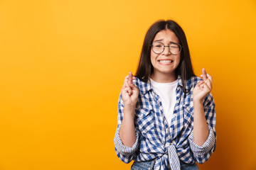 Wall Mural - Nervous emotional young cute teenage girl in glasses posing isolated over yellow wall background showing hopeful please gesture.