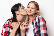 Positive Optimistic Young Pretty Girls Friends Sisters Posing Isolated Over White Wall Background Holding Pinky Of Each Other Kissing Cheek.
