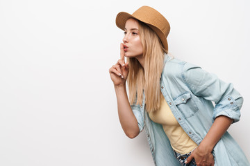 Poster - Serious amazing young pretty woman wearing hat posing isolated over white wall background showing silence gesture.