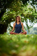 © chika_milan - Smiling Caucasian woman in sports clothing sitting on mat in nature and meditating.