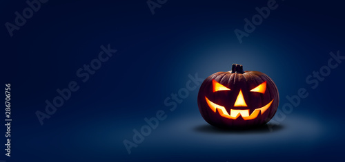 Fotomural A halloween lit Jack O Lantern in a spotlight glow on a wide dark blue backgroun