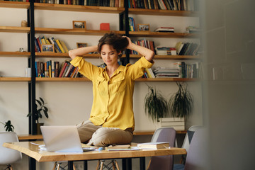 Aufkleber - Young attractive woman in yellow shirt sitting on desk while dreamily working on laptop in modern office