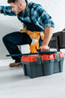 © LIGHTFIELD STUDIOS - bearded handyman in uniform sitting and holding toolbox