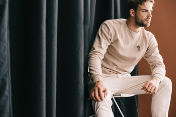 Wall Mural - man in casual outfit sitting on chair near curtain on brown