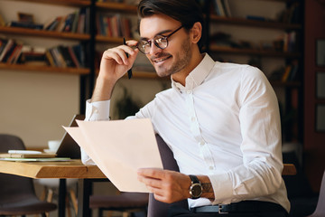 Aufkleber - Young smiling businessman in eyeglasses and white shirt happily working with papers in office