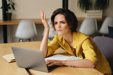 Aufkleber - Young upset businesswoman sitting at the desk with laptop thoughtfully looking aside at work in office