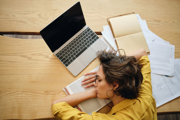 Aufkleber - Top view of young tired woman asleep on desk with laptop and documents under head at workplace