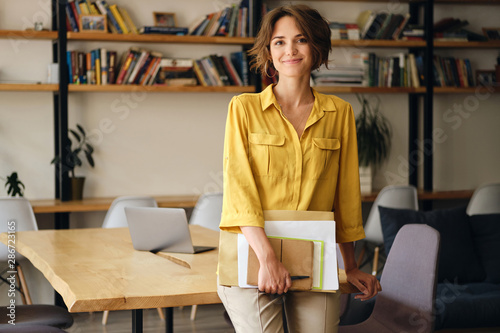 Fotomural Young beautiful woman in yellow shirt leaning on desk with notepad and papers in