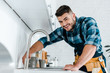 © LIGHTFIELD STUDIOS - selective focus of happy handyman working near sink in kitchen