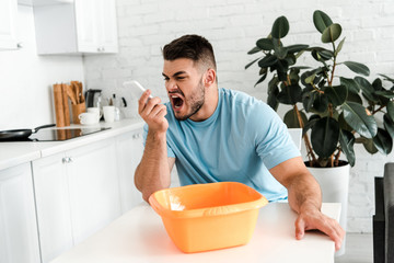 Poster - selective focus of upset bearded man screaming at smartphone near plastic wash bowl