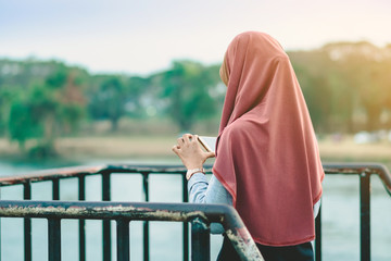 Wall Mural - Back view of Muslim woman relax and admire the beautiful scenery in the evening on The Bridge of the River Kwai in Kanchanaburi, Thailand.