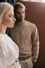 Wall Mural - selective focus of attractive blonde girl and bearded young man with hand in pocket on brown