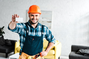 Wall Mural - cheerful worker holding blank card and standing with hand on hip