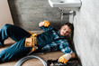© LIGHTFIELD STUDIOS - bearded handyman lying on floor near toolbox in bathroom