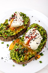 Wall Mural - Poached eggs with avocado guacomole on brown bread with sesame seeds. Healthy breakfast on a white background.