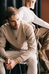 Wall Mural - blonde woman in white blouse and bearded man sitting on chair near curtain