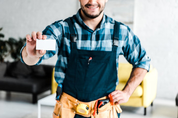 Wall Mural - cropped view of cheerful worker holding blank card and standing with hand on hip